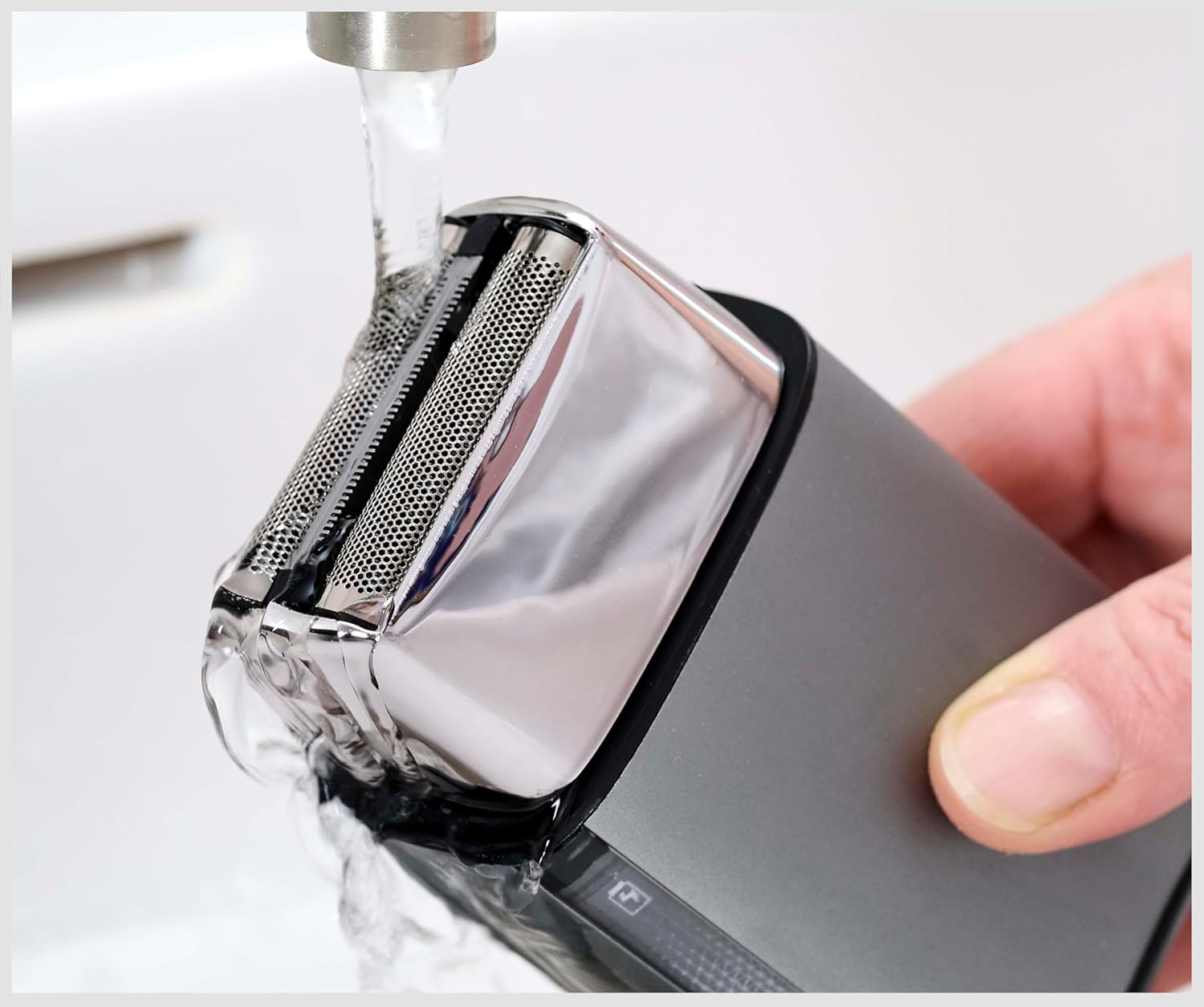 Egy elektromos borotvát öblítenek le a csapból folyó víz alatt.