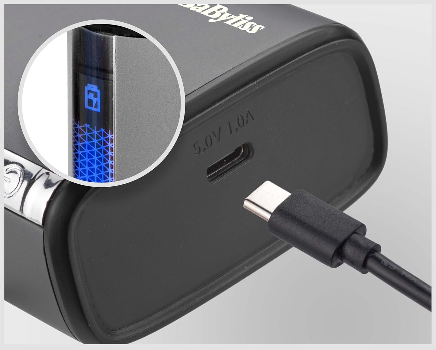 Egy USB-C kábel csatlakozik egy fekete eszköz töltőportjához, akkumulátor-kijelzővel egy kör alakú részletben.