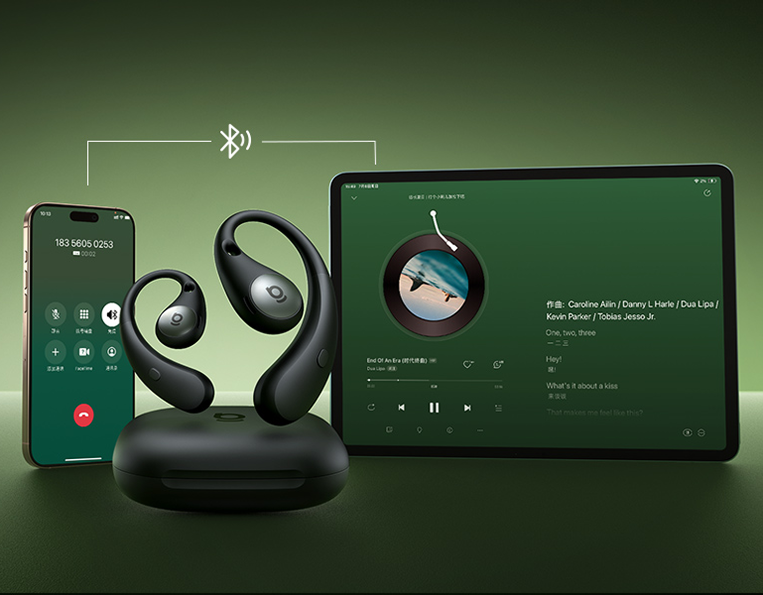 Auriculares Bluetooth negros en estuche de carga, conectados a un smartphone y una tablet sobre fondo verde.