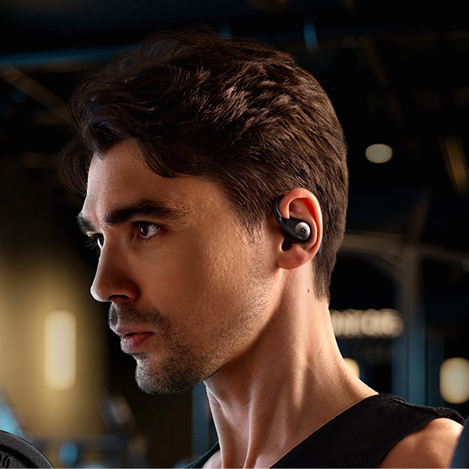 Un hombre con cabello castaño corto lleva un pequeño auricular negro en un gimnasio.