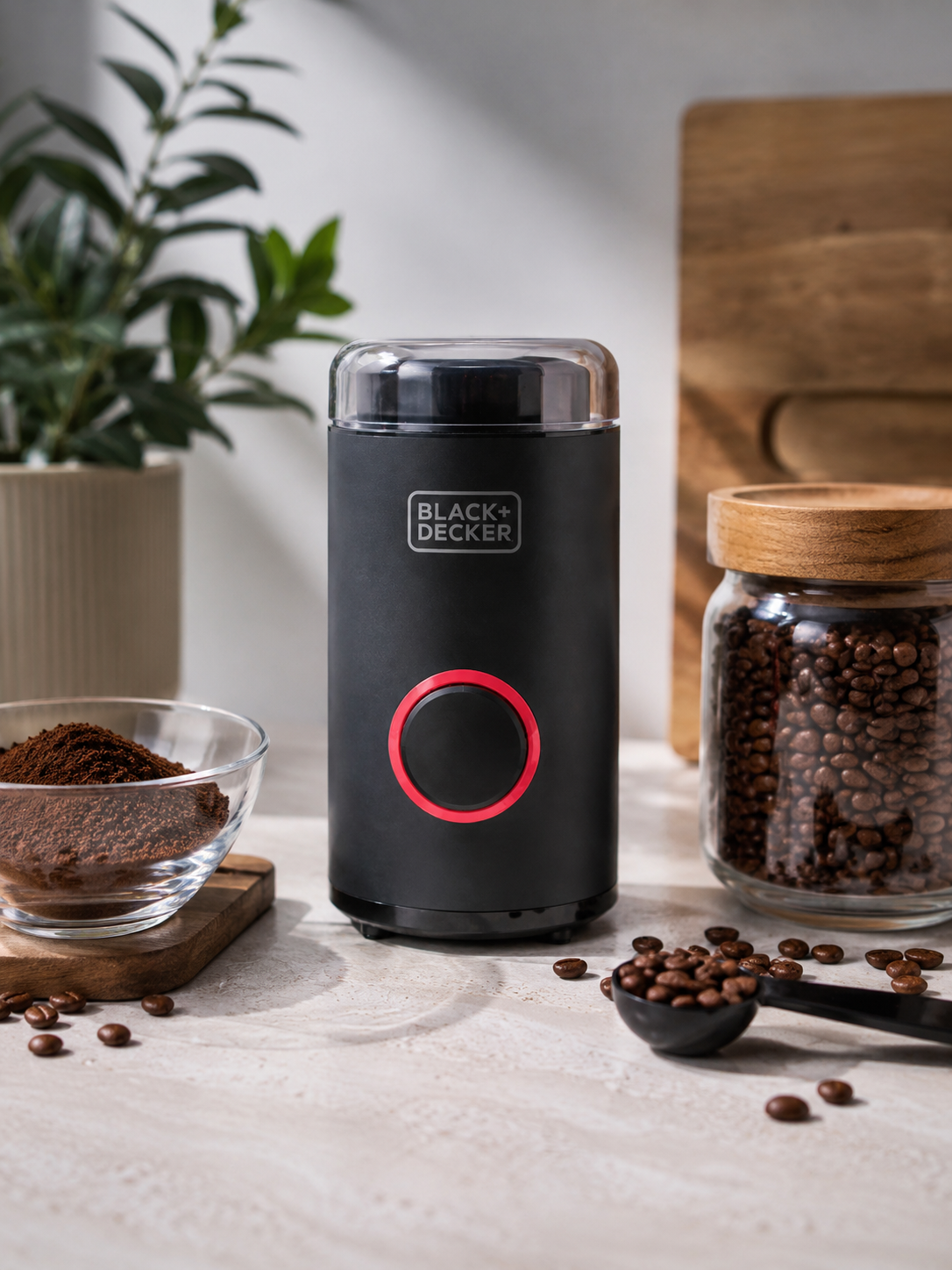 Czarny młynek do kawy Black+Decker na blacie z ziarnami, mieloną kawą i szklanym słoikiem.