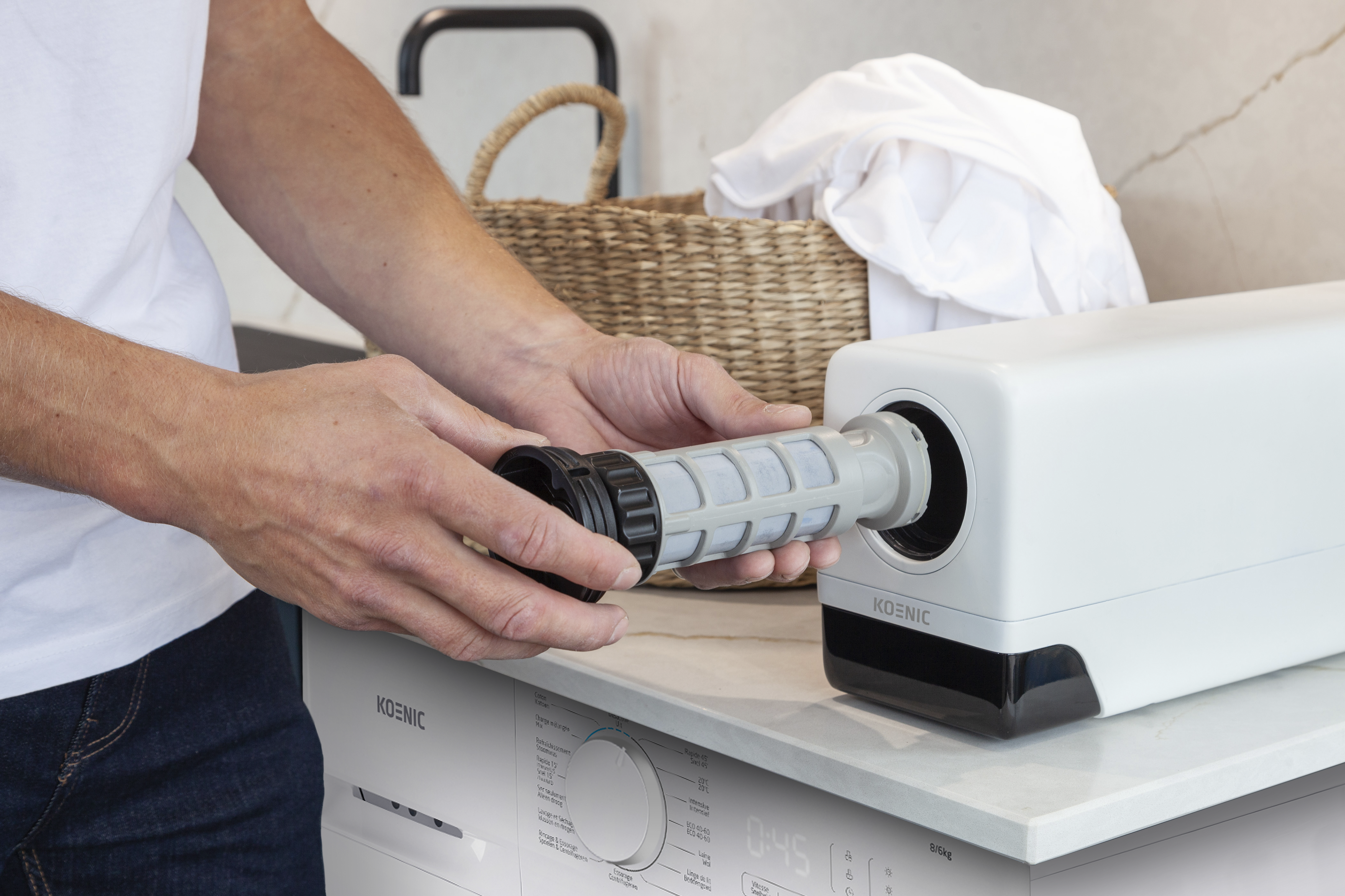 Eine Person zieht einen zylindrischen grauen Filter aus einer weißen Maschine auf einer Waschmaschine heraus.