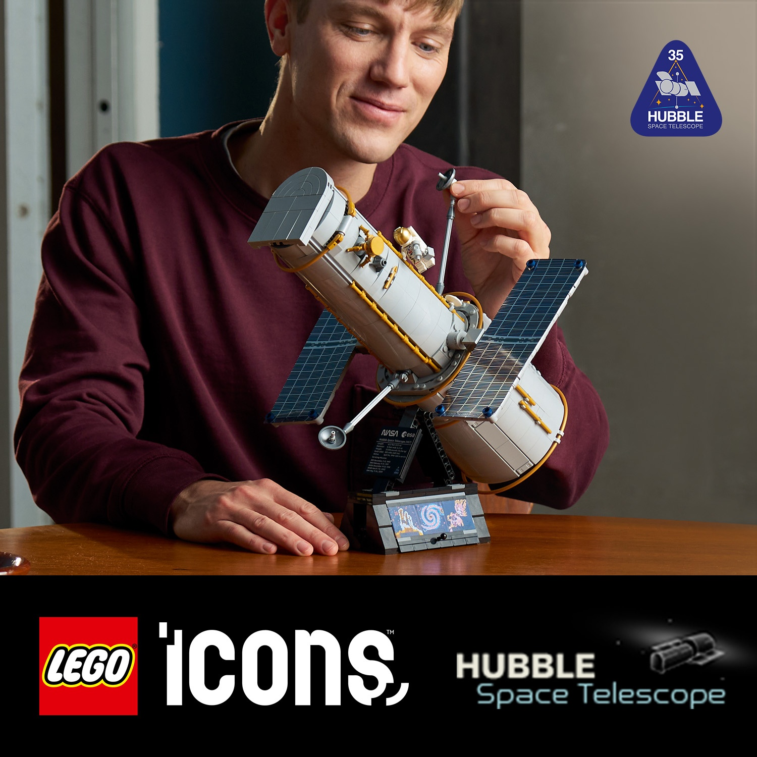 Un uomo con una camicia bordeaux assembla un dettagliato modello Lego del telescopio spaziale Hubble.