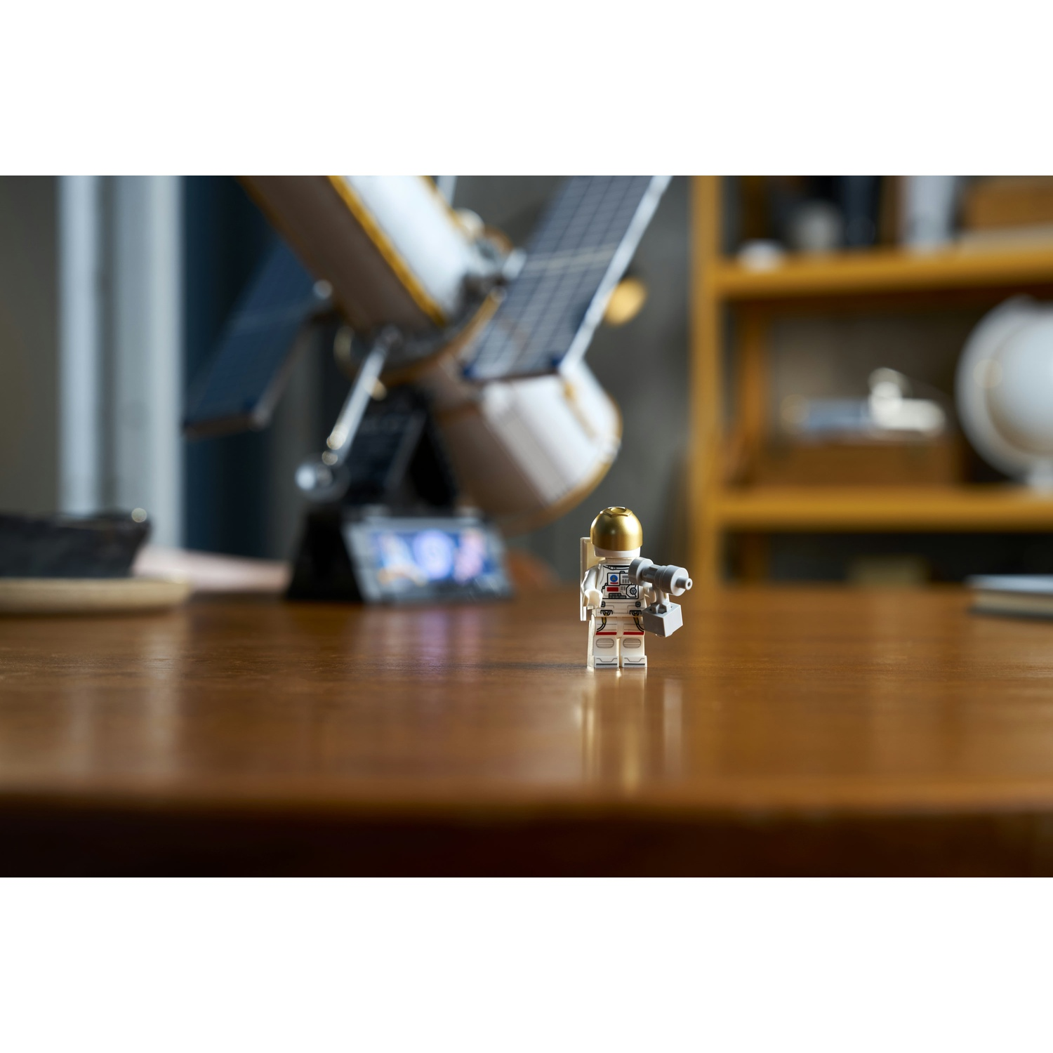 Un astronauta Lego si trova su un tavolo di legno, con un modello di satellite sullo sfondo.