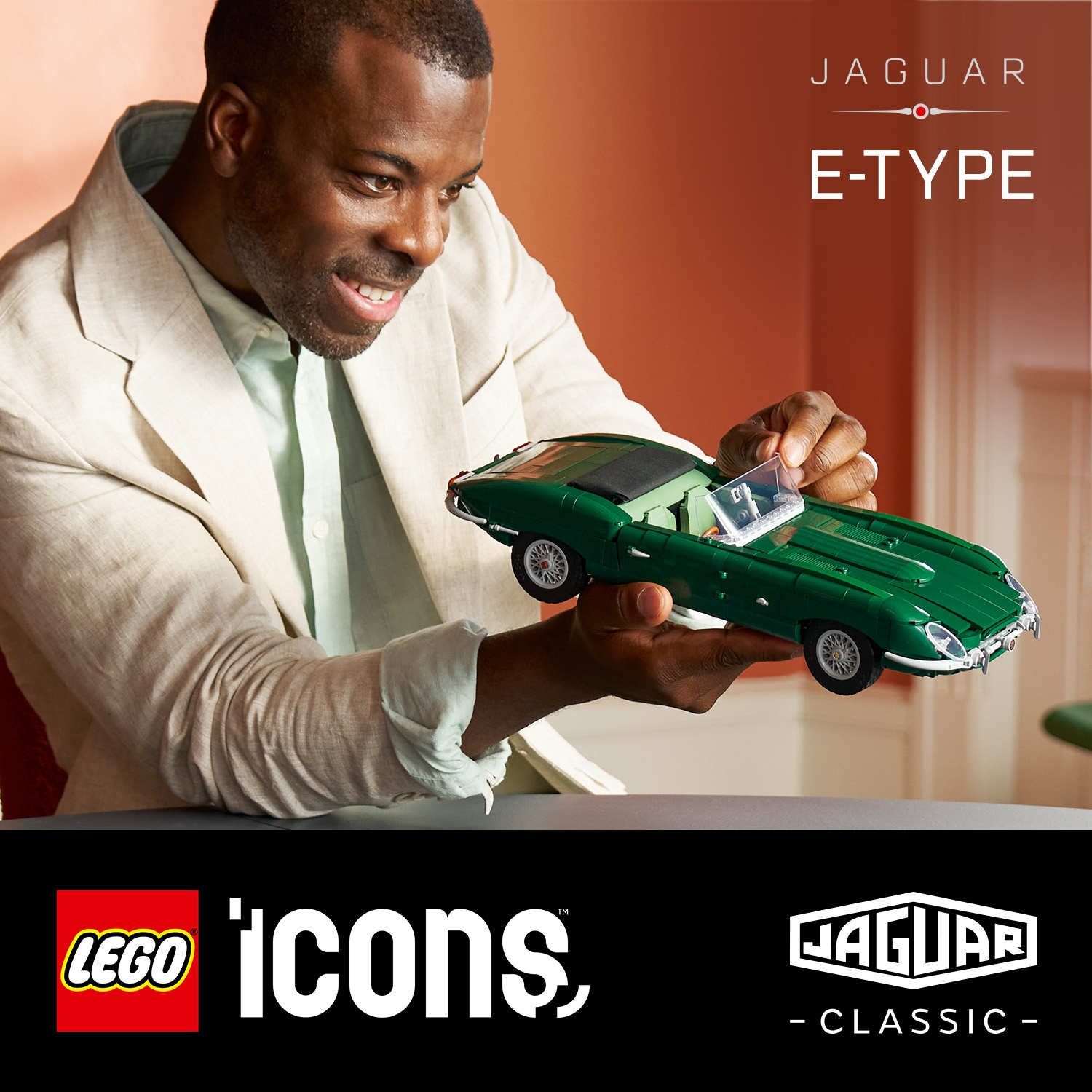 Un uomo sorridente in blazer chiaro tiene con orgoglio un'auto modello Lego Jaguar E-Type verde.