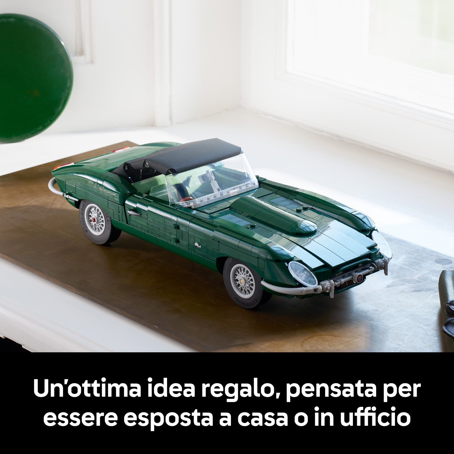 Un'auto cabrio in Lego verde si trova su un tavolo di legno vicino a una finestra.