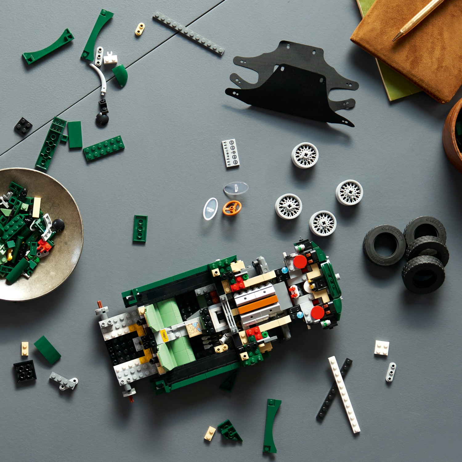 Un'auto Lego verde incompleta si trova su un tavolo grigio, circondata da pezzi sfusi e ruote.
