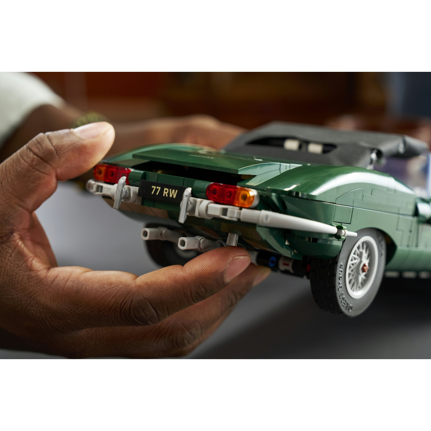 Mani che tengono la parte posteriore di un'auto classica Lego verde con targa 77 RW.