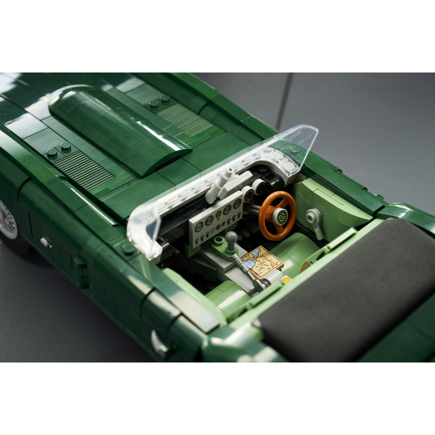 Vista dall'alto di un'auto cabrio Lego verde, con abitacolo e volante dettagliati su sfondo grigio.