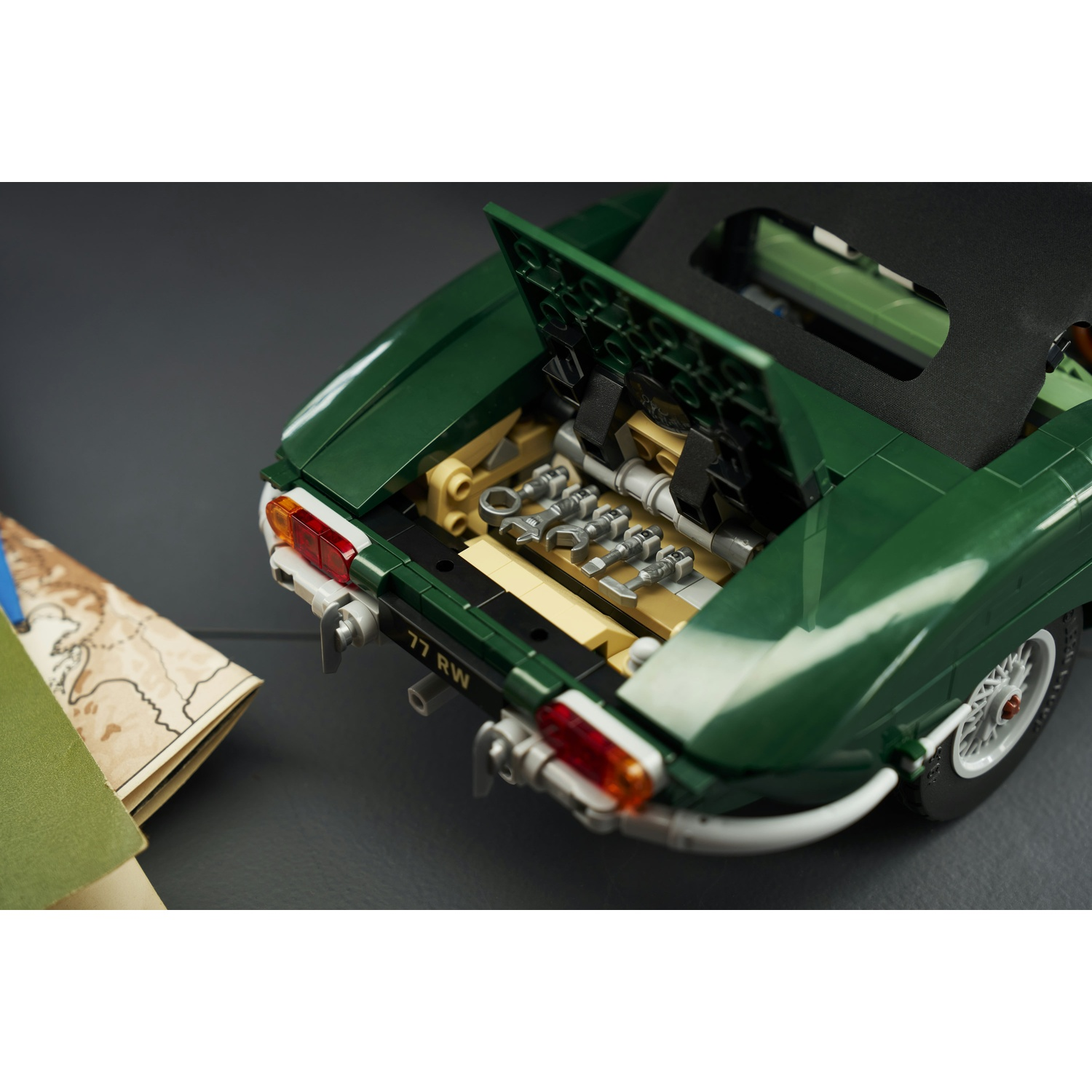 Un'auto giocattolo LEGO verde con il bagagliaio aperto, che mostra attrezzi all'interno, accanto a una mappa su una superficie scura.