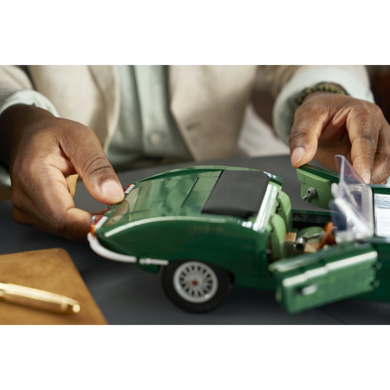 Le mani assemblano un'auto giocattolo verde con le porte aperte su un tavolo grigio.