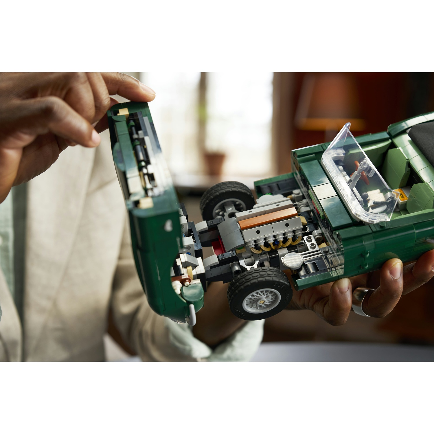 Una persona apre il cofano di un'auto giocattolo verde LEGO per rivelare il motore.