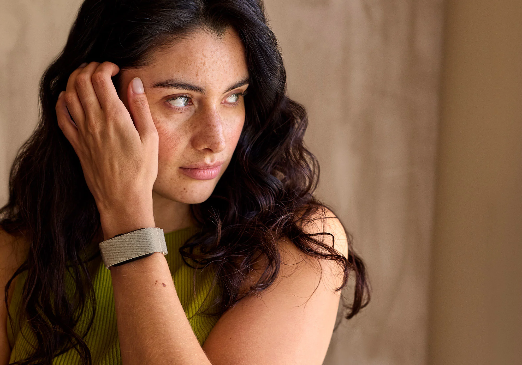Une femme aux cheveux noirs bouclés touche sa joue et porte un bracelet au poignet.