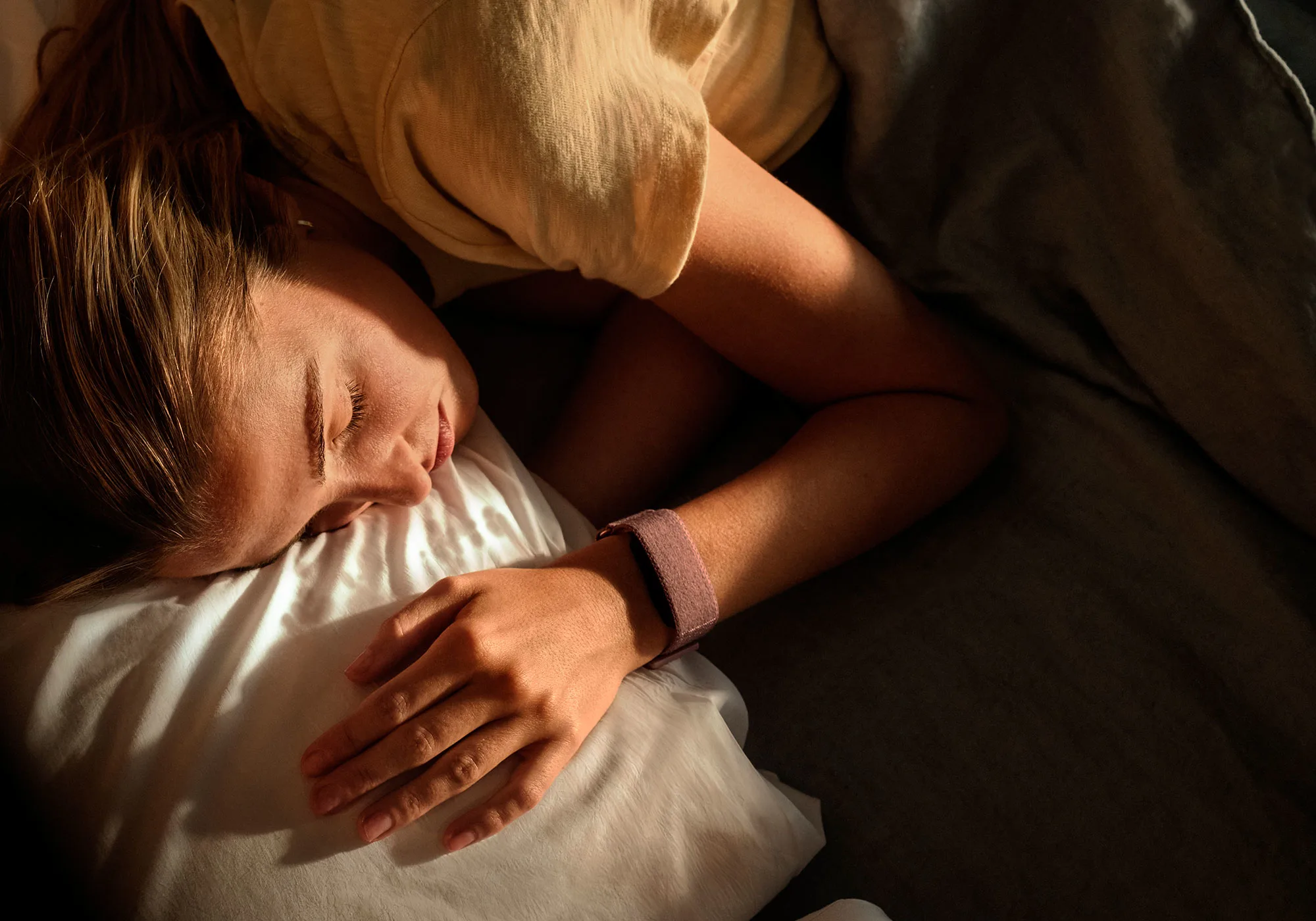 Une femme dort paisiblement sur un oreiller blanc, portant un bracelet connecté.