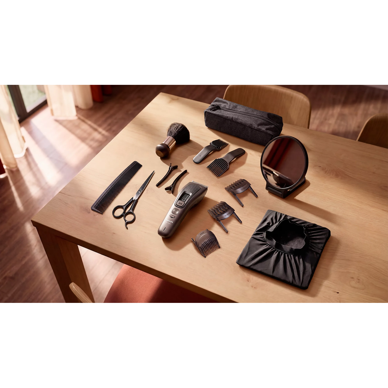 Een houten tafel toont tondeuse, schaar, kam, borstel, opzetstukken, spiegel en zwarte cape.