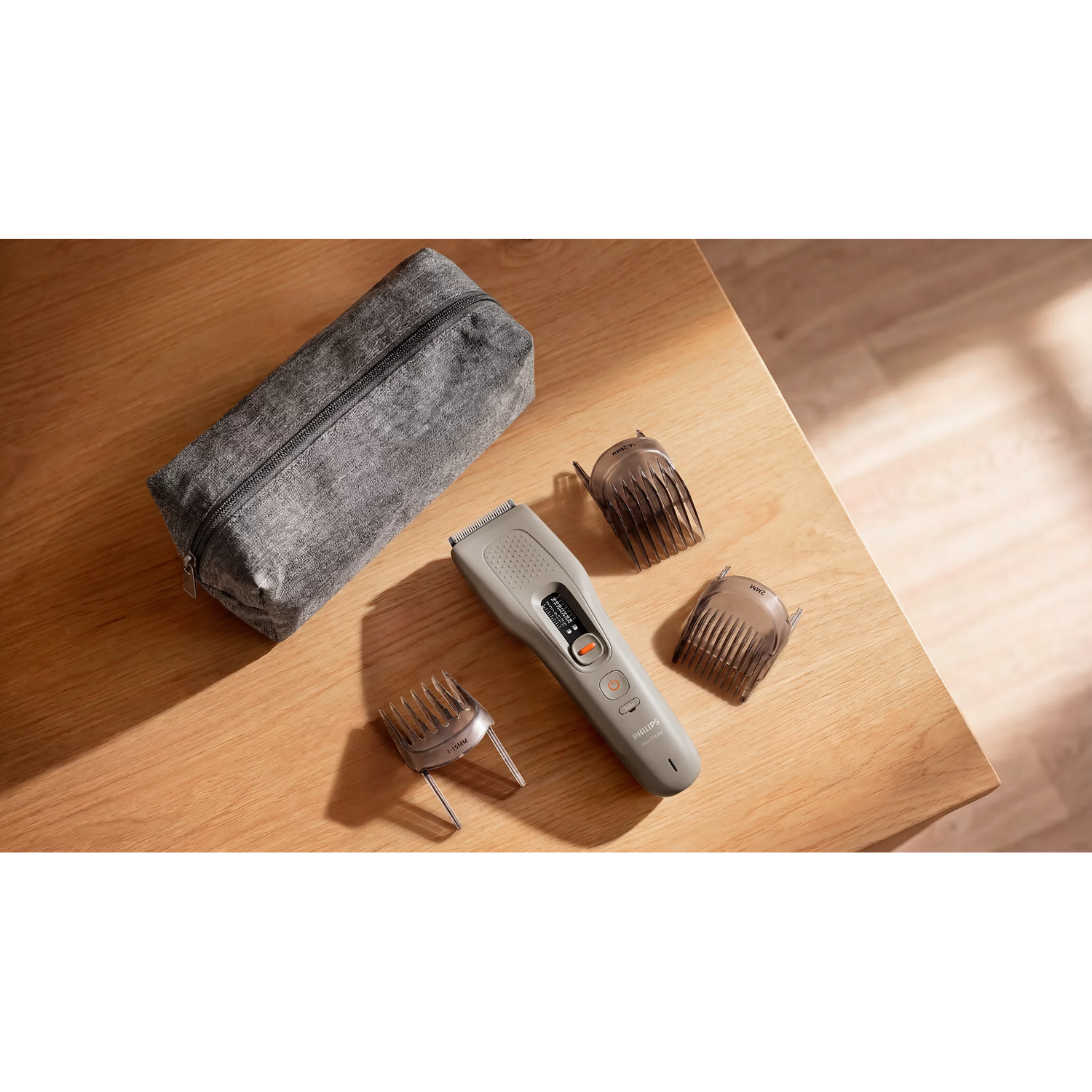 Une tondeuse à cheveux Philips avec trois sabots noirs et une pochette grise disposés sur une table en bois.