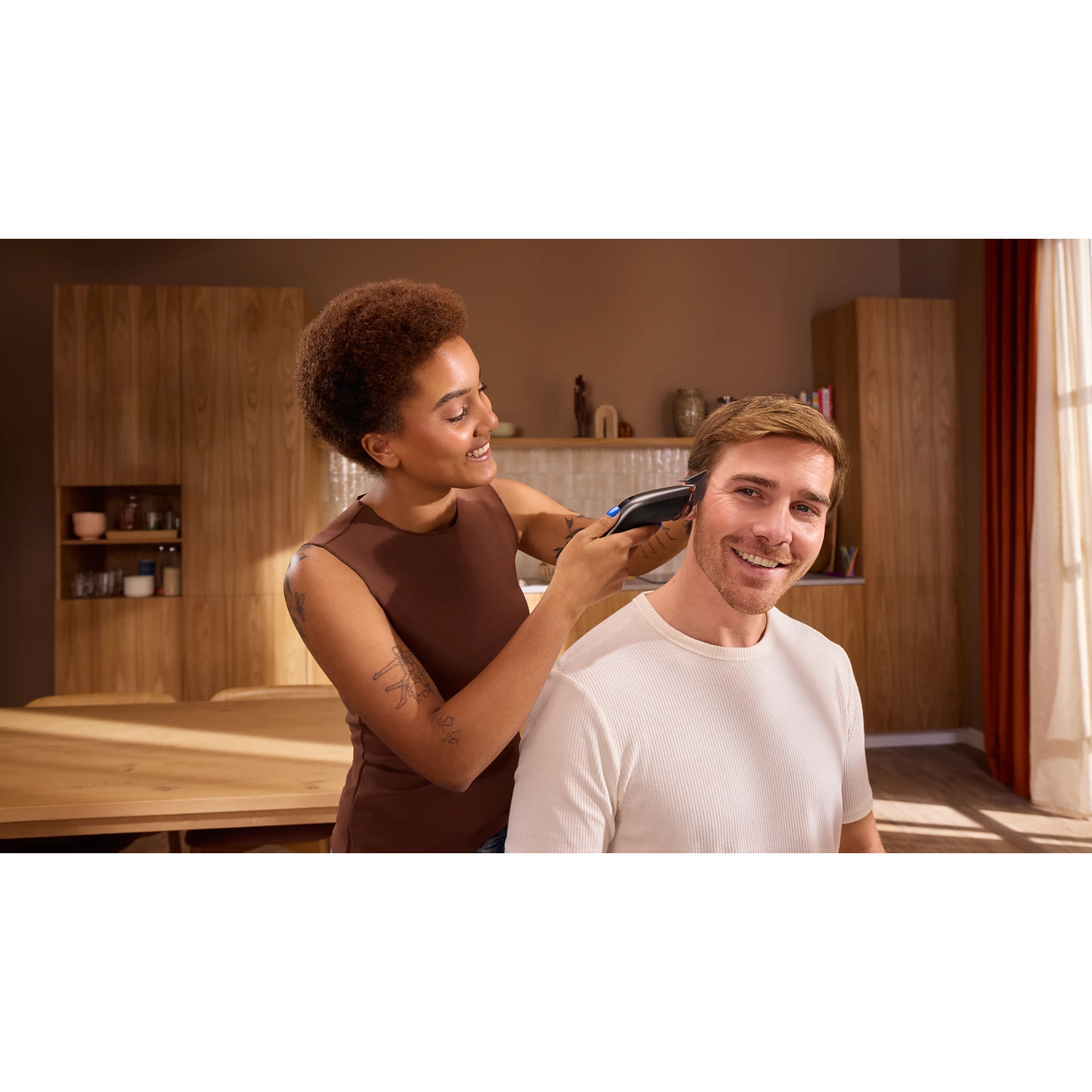 Une femme coupe les cheveux d'un homme souriant à la maison à l'aide d'une tondeuse à cheveux.