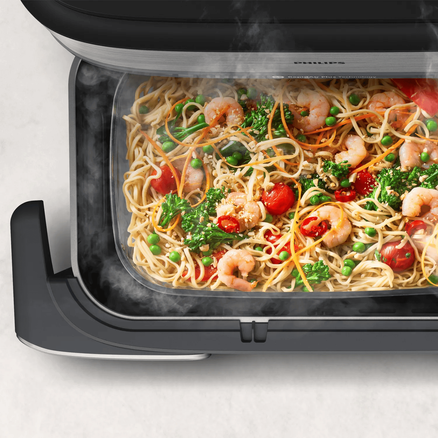 Plat fumant de nouilles, crevettes, petits pois, brocoli et tomates dans un appareil.
