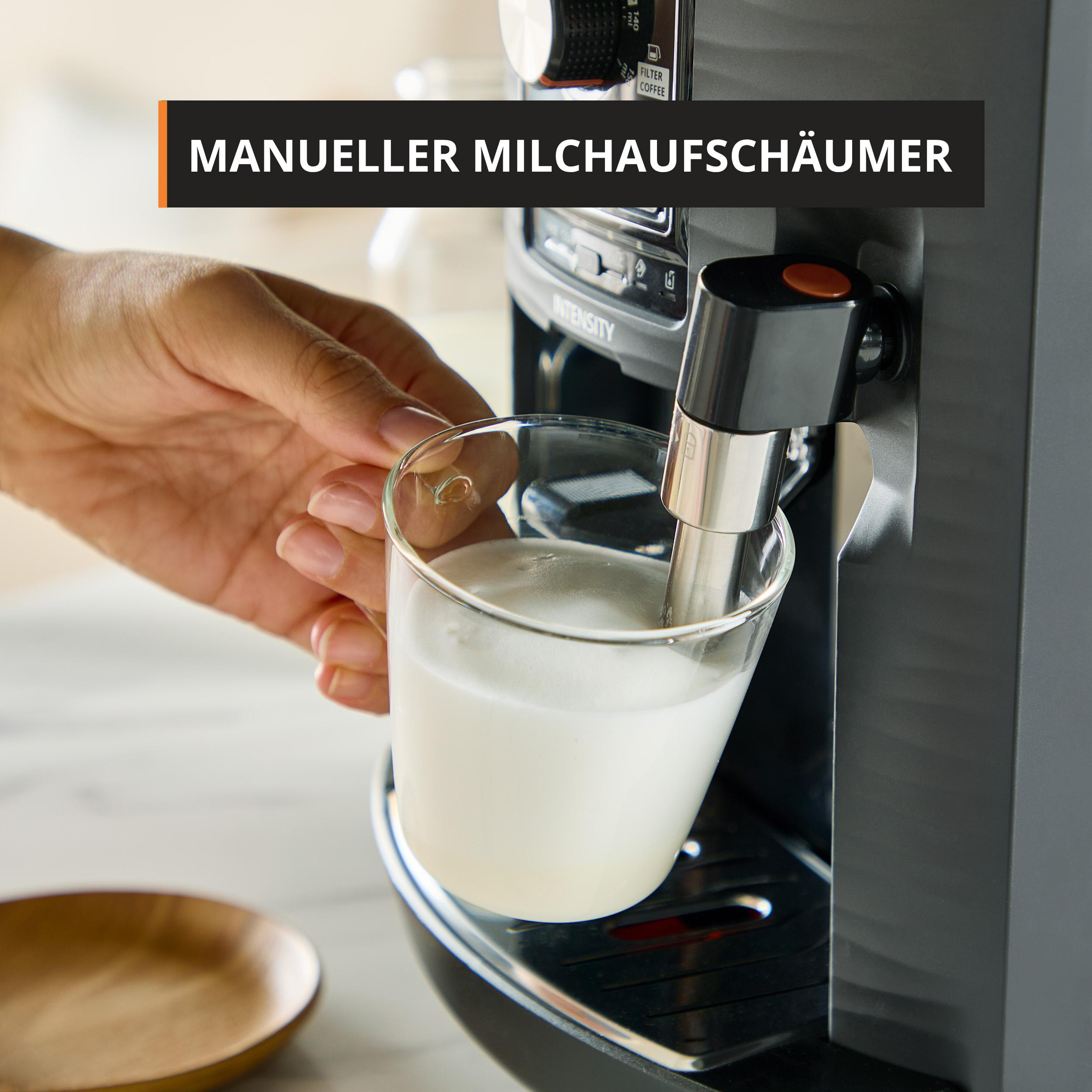 Hand hält eine Glastasse mit Milch unter die Dampfdüse einer Kaffeemaschine.