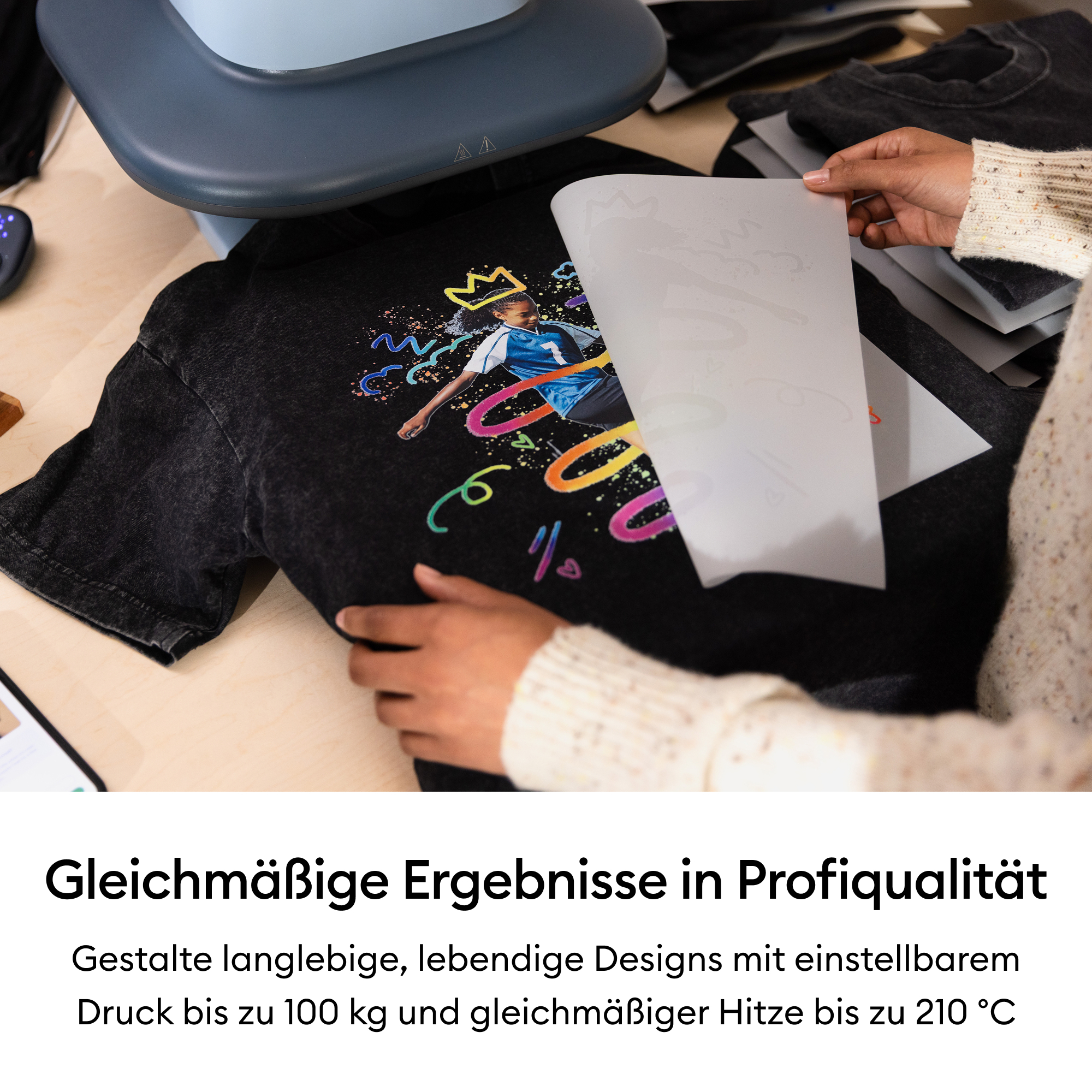 Eine Person zieht Transferpapier vorsichtig von einem frisch gedruckten, bunten Motiv ab.