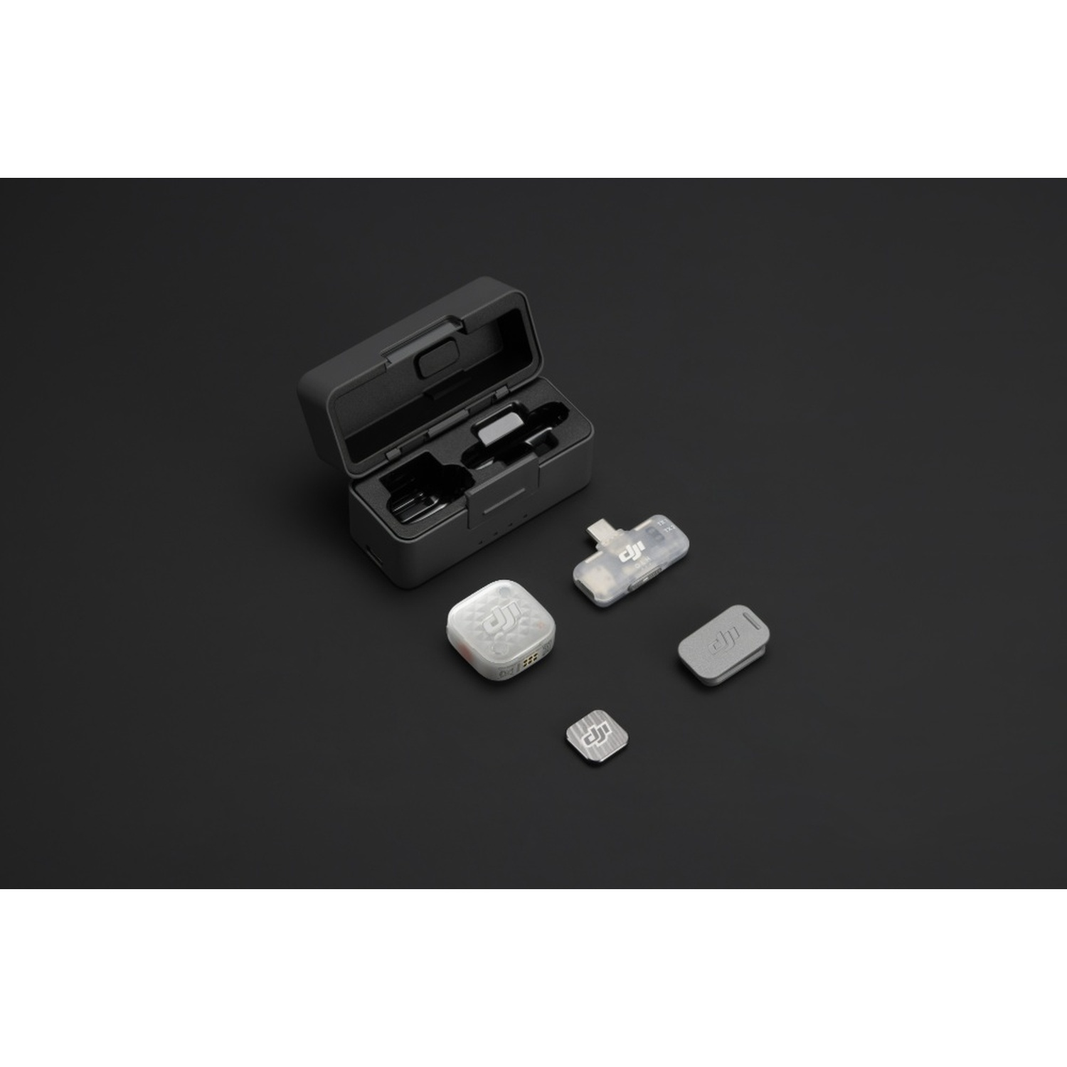 Una custodia di ricarica nera aperta e componenti microfonici DJI wireless su una superficie scura.