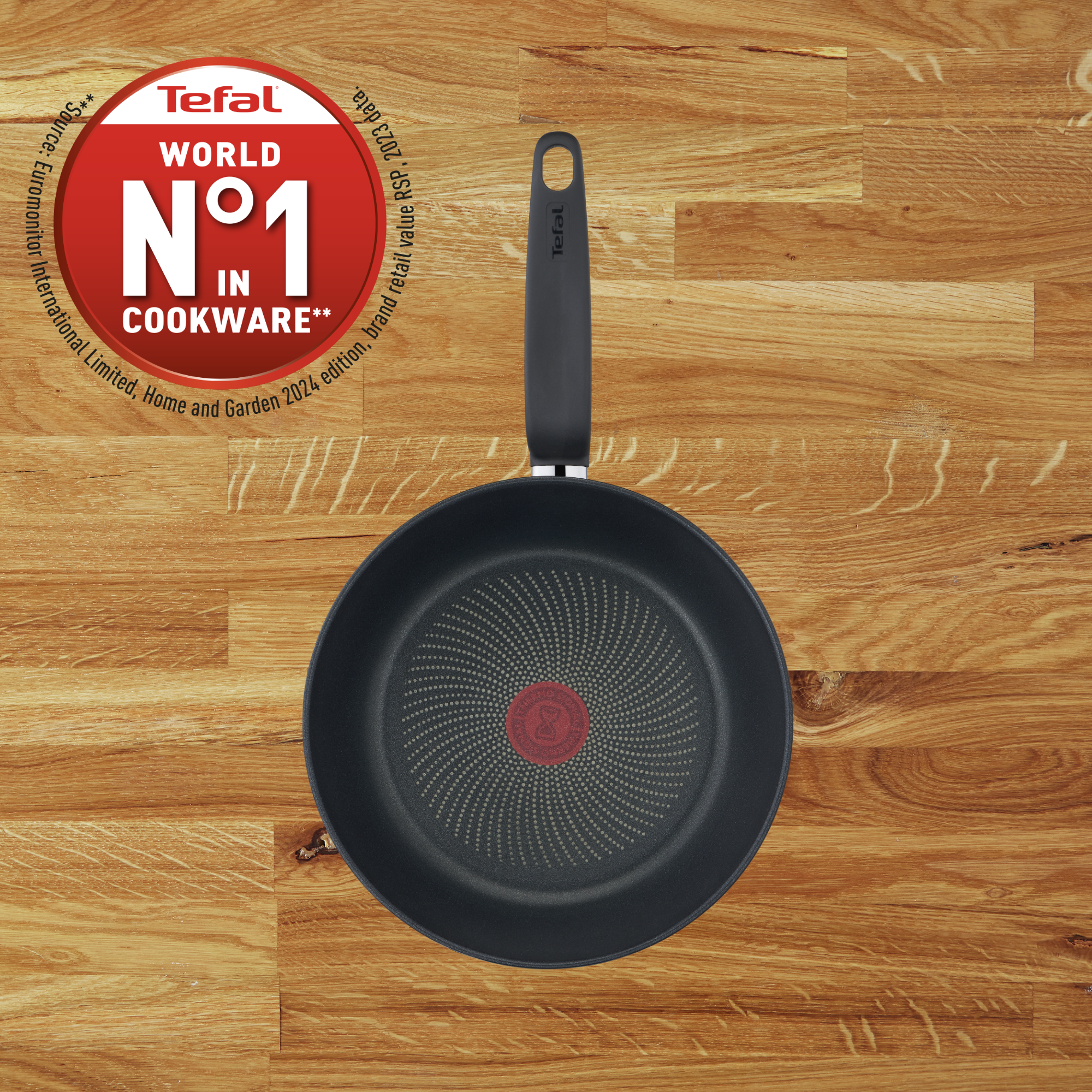 Una sartén negra Tefal con indicador rojo de calor en superficie de madera.