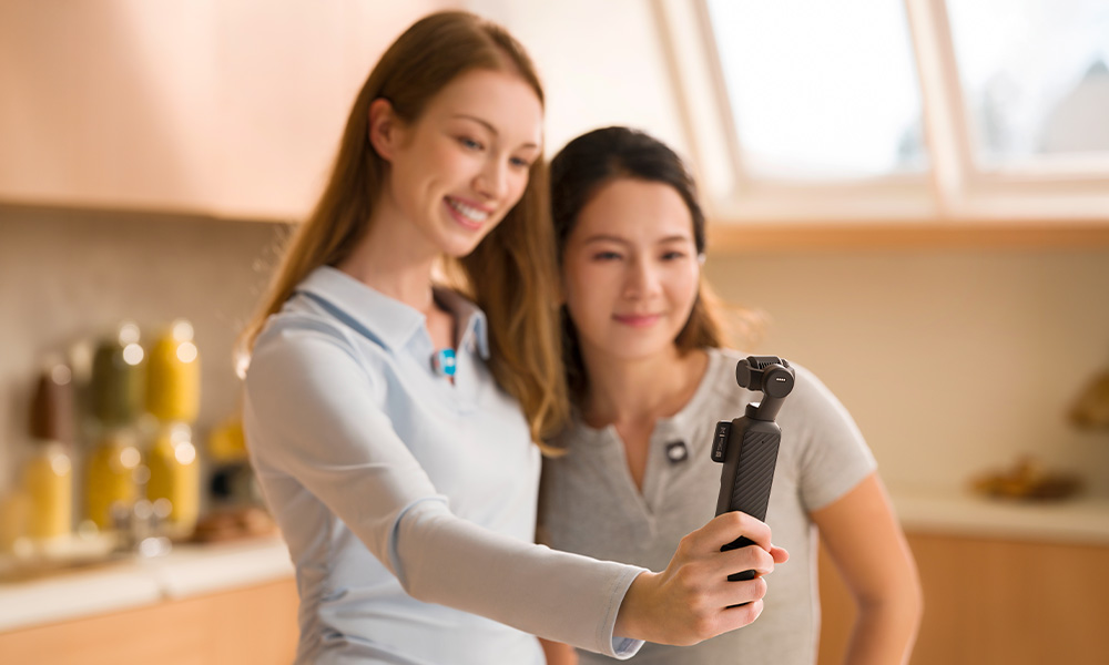 Dwie uśmiechnięte kobiety robią sobie selfie małą kamerą z gimbalem w kuchni.
