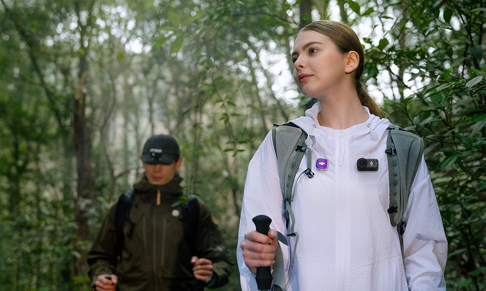 Kobieta w białej kurtce i mężczyzna wędrują po zielonym lesie z kijkami trekkingowymi.