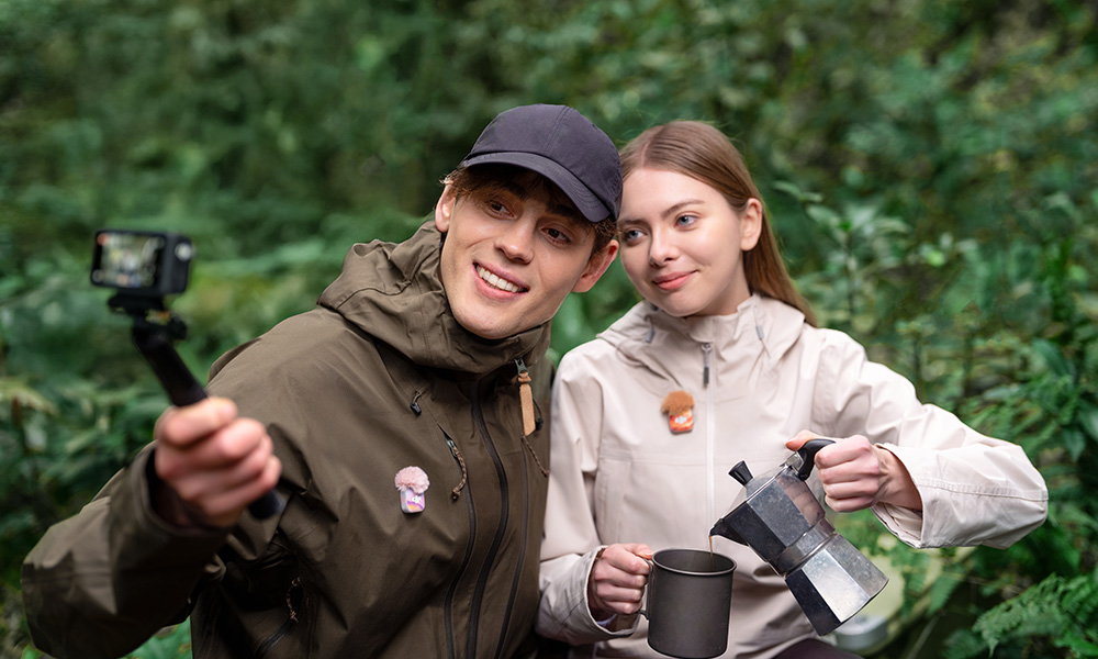 Para biwakuje w lesie, gdy on robi sobie selfie aparatem, a ona nalewa kawę z kawiarki.