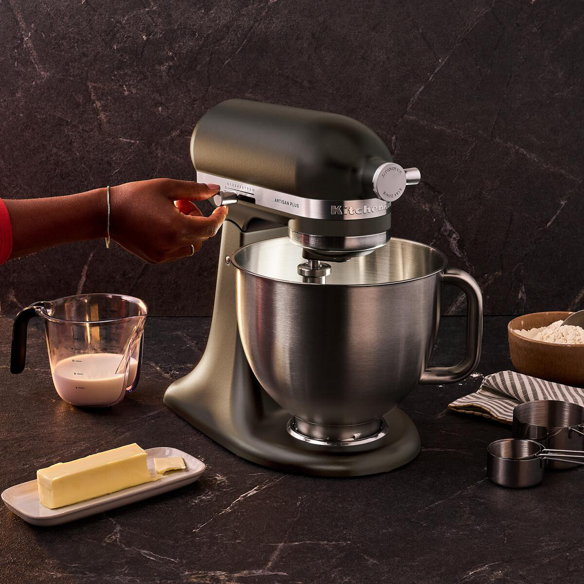 Eine Hand bedient einen dunkelgrauen Standmixer auf einer dunklen Marmorarbeitsplatte.