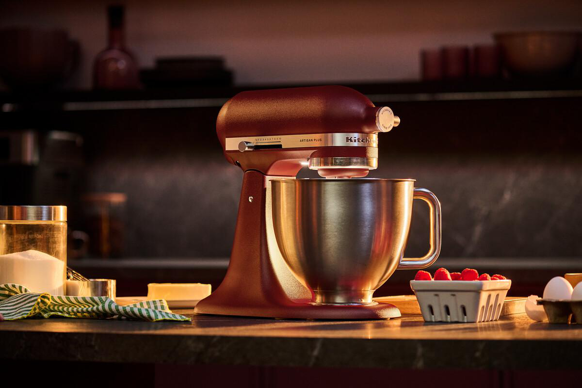 Eine dunkelrote KitchenAid-Küchenmaschine steht auf einer Küchentheke mit Beeren und Eiern.