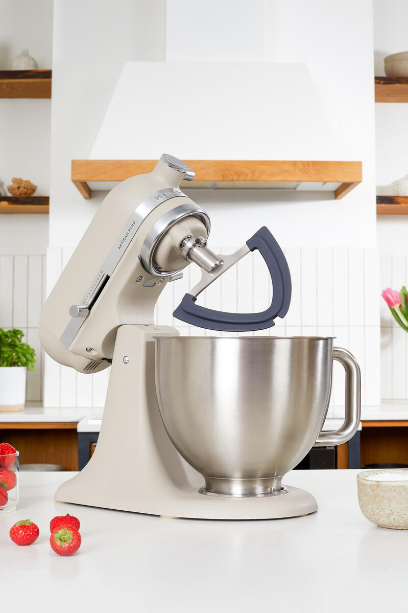 Eine beigefarbene Küchenmaschine mit Edelstahlschüssel auf einer weißen Arbeitsplatte, mit frischen Erdbeeren im Vordergrund.