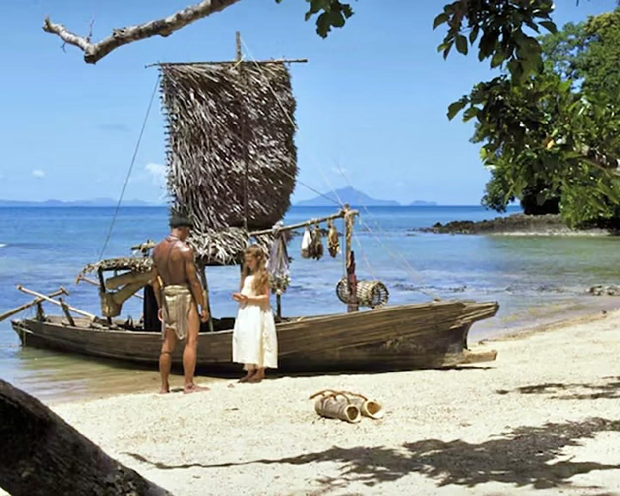 Ein Mann und ein Kind stehen an einem Sandstrand neben einem hölzernen Segelboot mit Strohsegel am blauen Ozean.