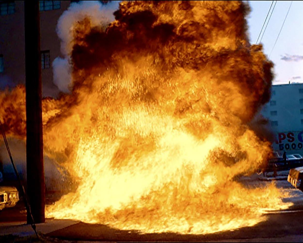 Eine riesige Explosion mit hellen gelben und orangen Flammen und dickem Rauch auf einer städtischen Straße.