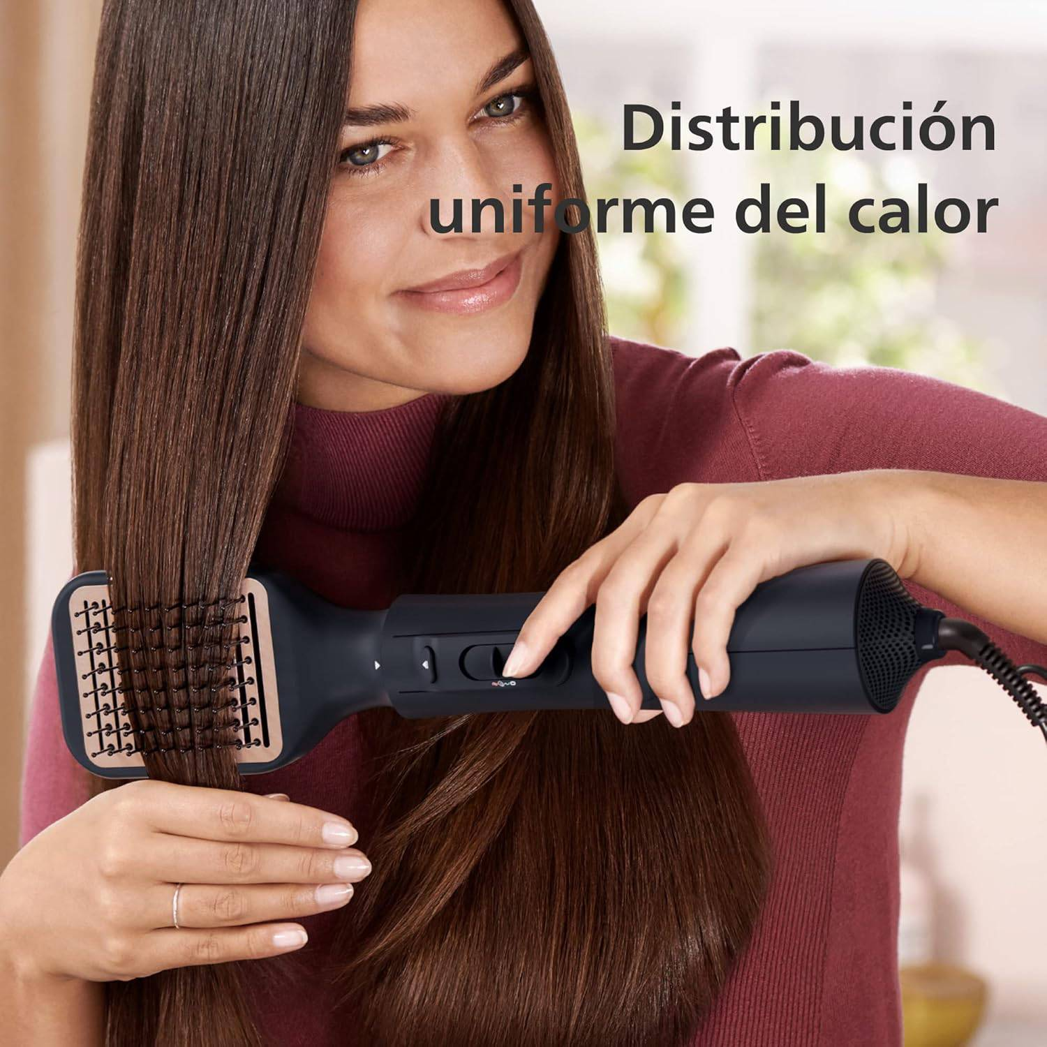 Una mujer sonríe mientras alisa su cabello castaño largo con un cepillo alisador.