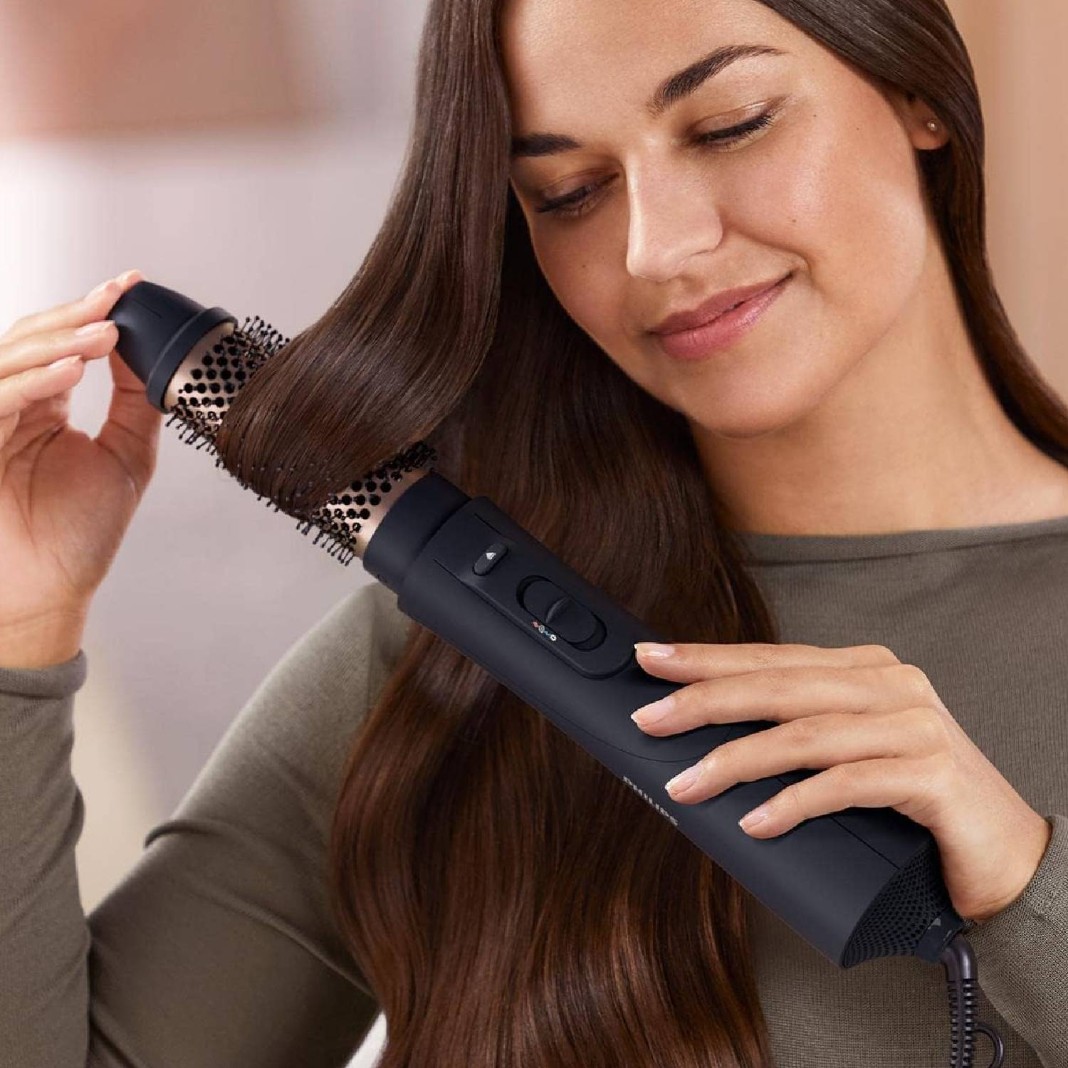 Una mujer peinando su cabello castaño con un moldeador de aire caliente negro.