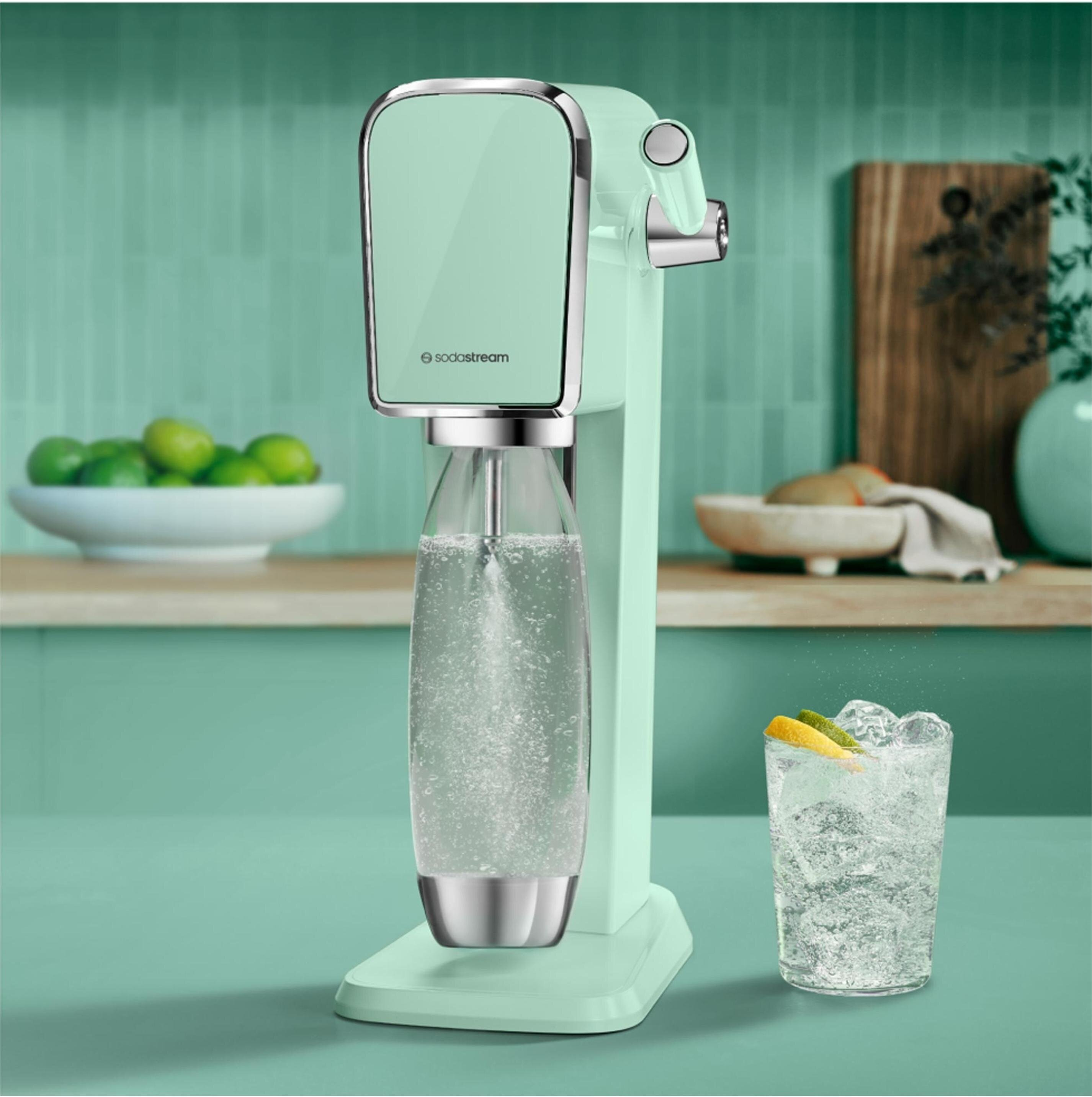 Miętowy ekspres do wody gazowanej SodaStream na blacie, obok szklanka lodu i plasterki cytrusów.