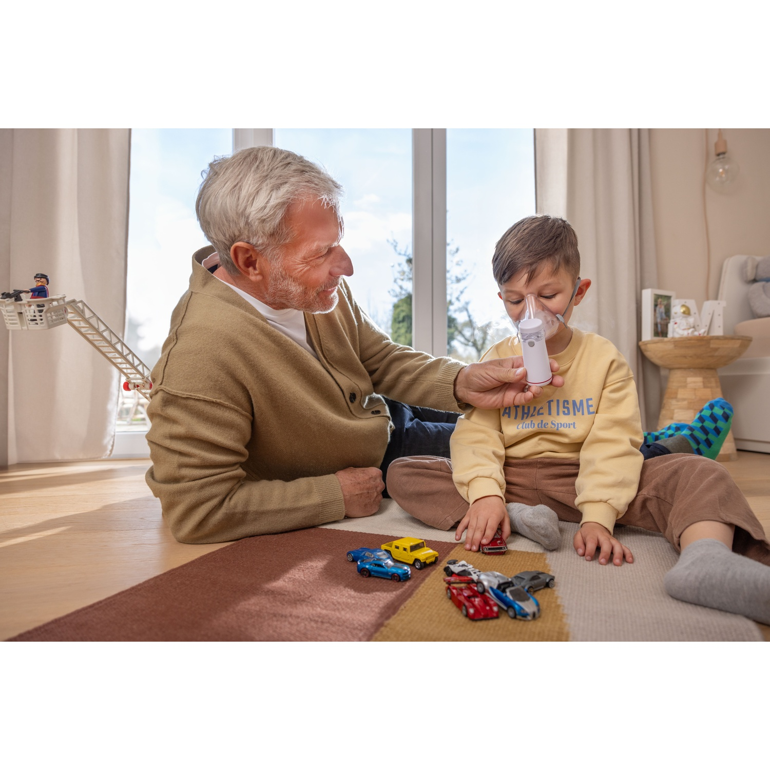 Il nonno siede sul tappeto con suo nipote, che usa un inalatore.