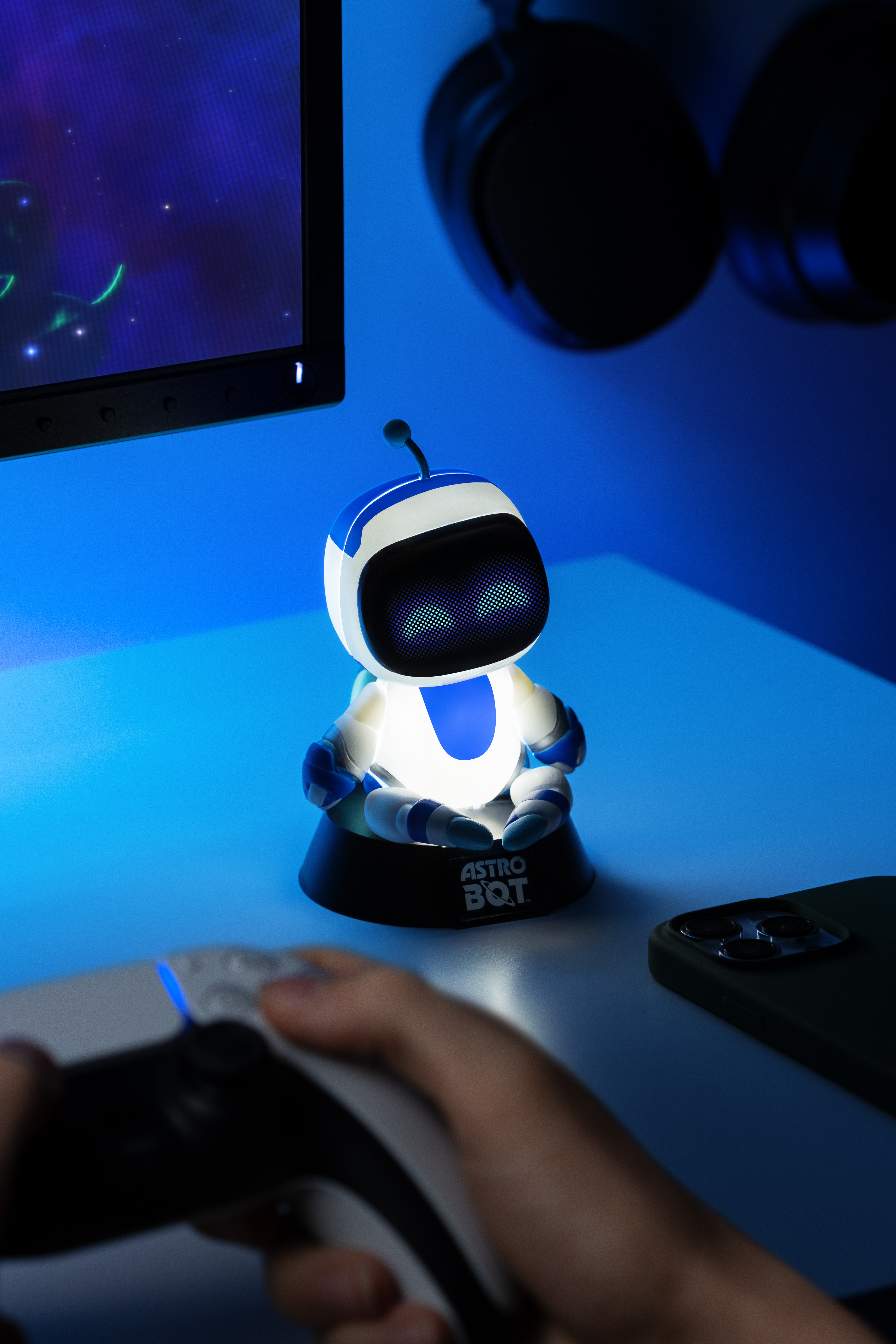 Beleuchtete Astro Bot-Figur auf einem Tisch mit einem Controller und Smartphone in der Nähe.