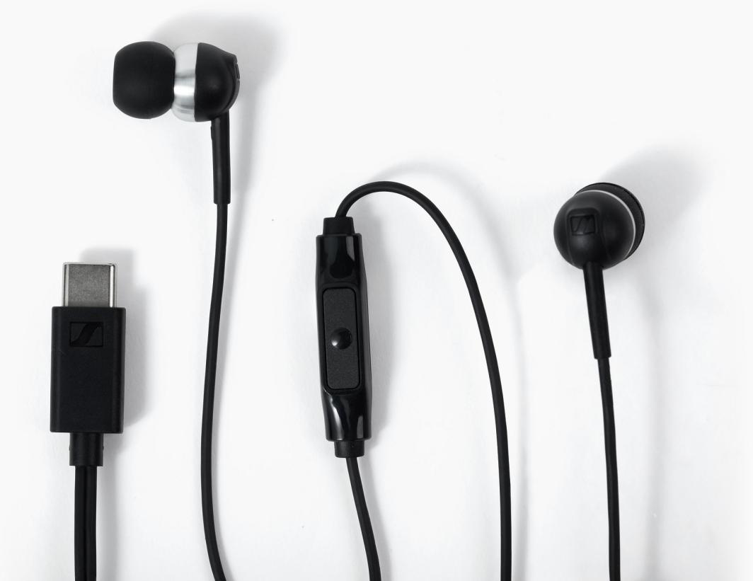 Fekete fülbe helyezhető fejhallgató USB-C csatlakozóval és beépített távirányítóval fehér háttéren.