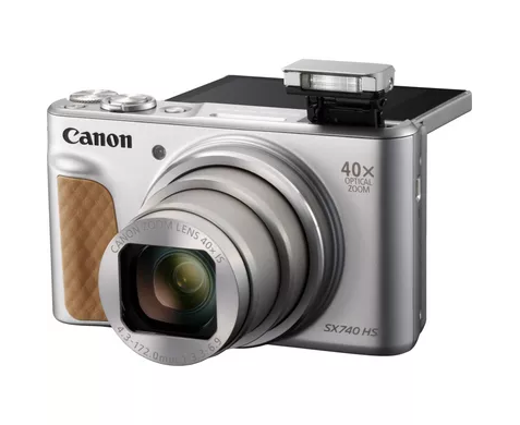 Srebrny aparat kompaktowy Canon SX740 HS z brązowym uchwytem, wysuniętym obiektywem i podniesioną lampą błyskową na białym tle.