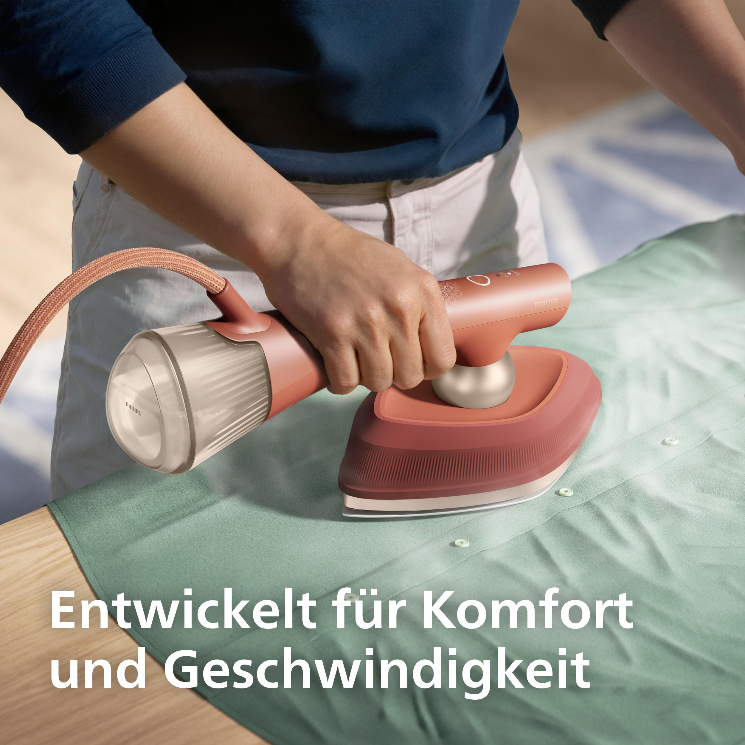 Eine Person bügelt ein grünes Hemd mit einem roten Philips-Dampfbügeleisen.