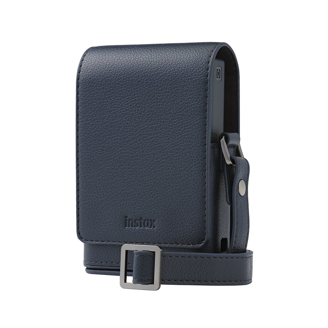 Beyaz arka planda metal tokalı ve kayışlı, koyu mavi dokulu deriden yapılmış Instax kamera kılıfı.