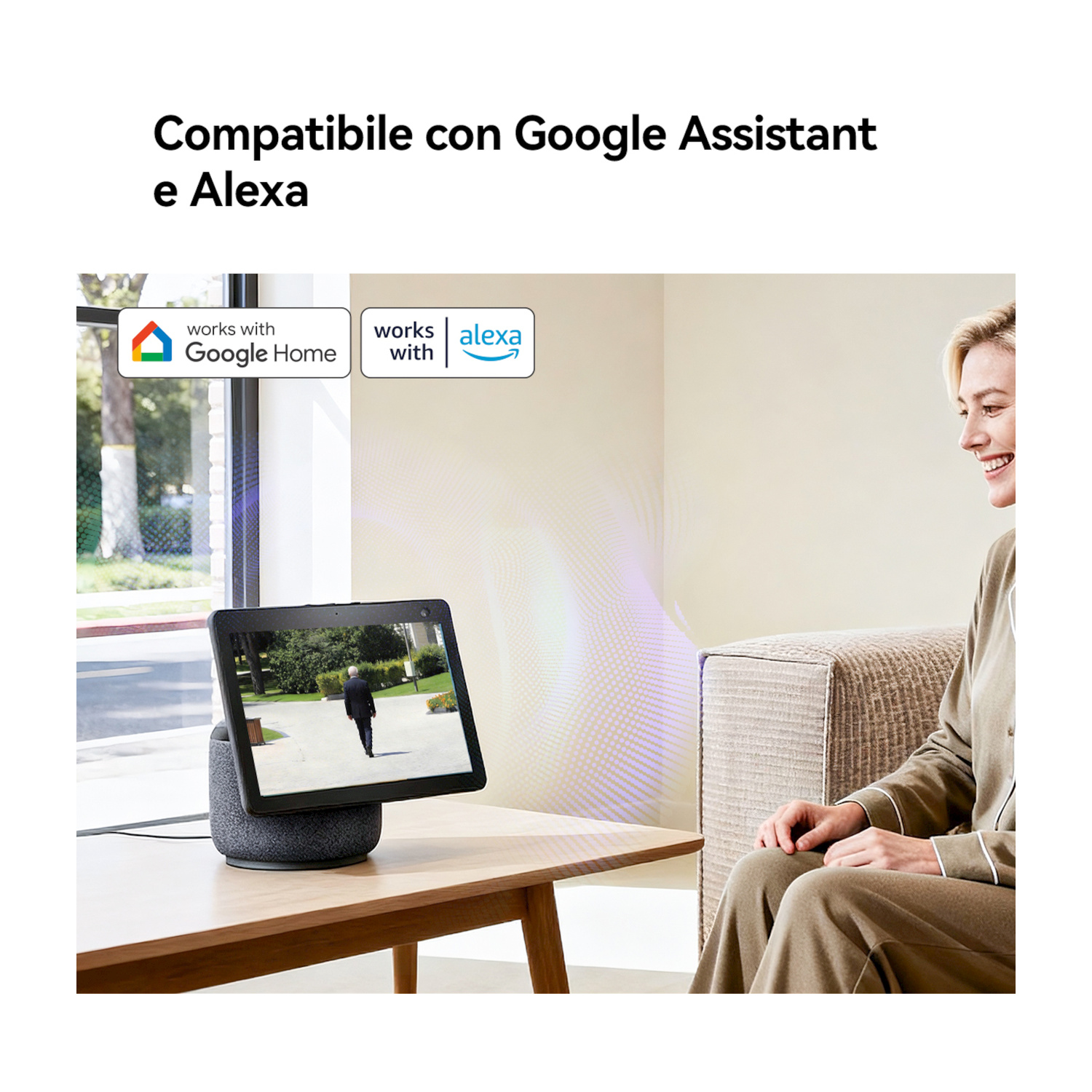 Una donna siede su un divano guardando uno smart speaker con schermo su un tavolo.