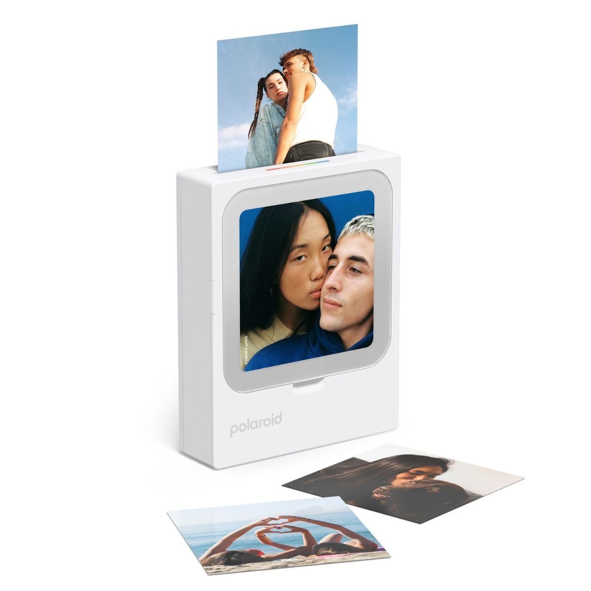 Ein weißer Polaroid-Drucker zeigt ein Paar, ein Foto kommt oben heraus und zwei liegen auf dem Boden.