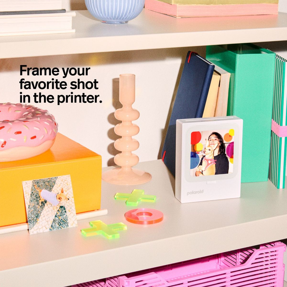Ein weißer Polaroid-Drucker steht auf einem Regal neben Dekorationen, Büchern und einer gedruckten Fotokarte.
