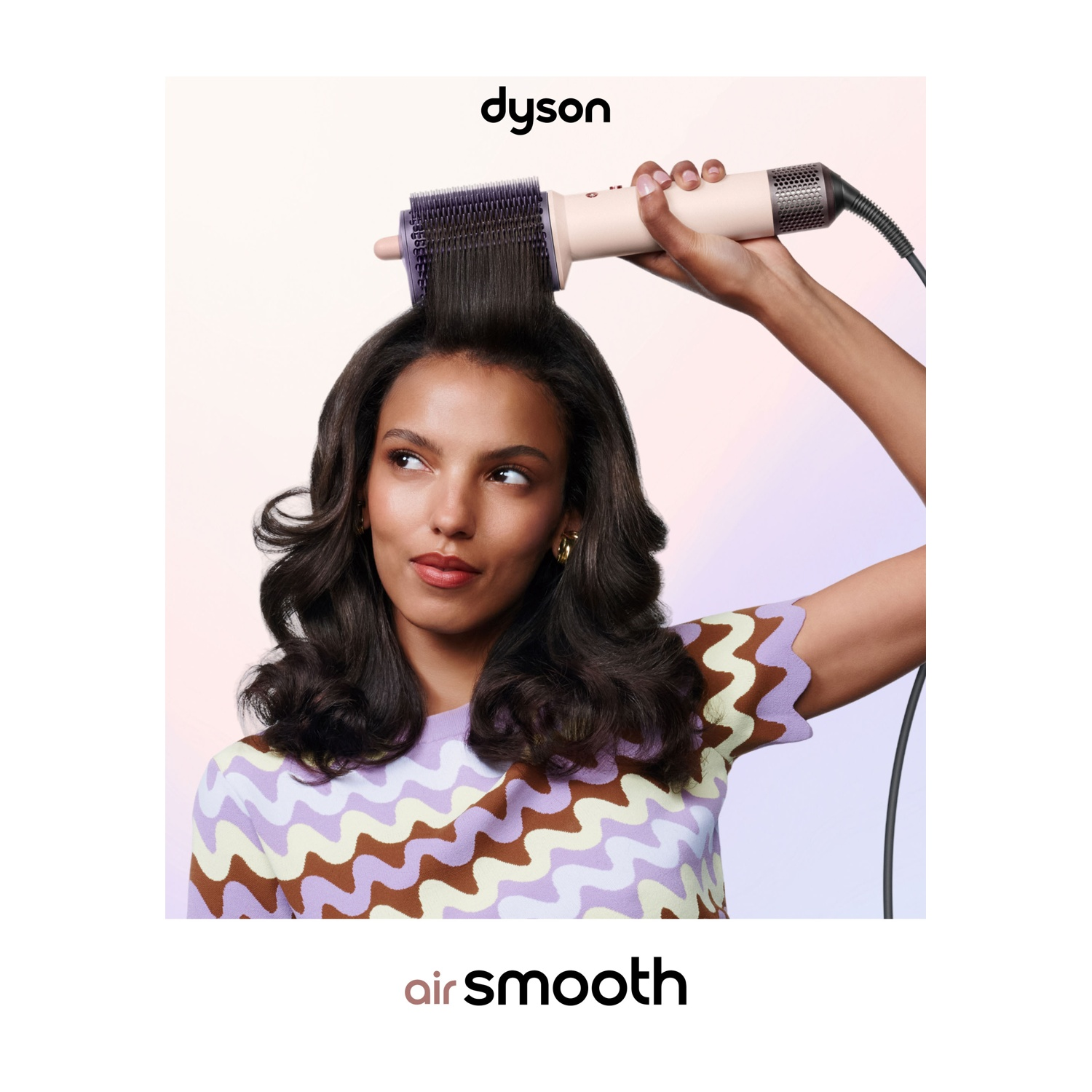 Una donna con capelli ondulati li modella usando un Dyson Airwrap rosa su uno sfondo chiaro.