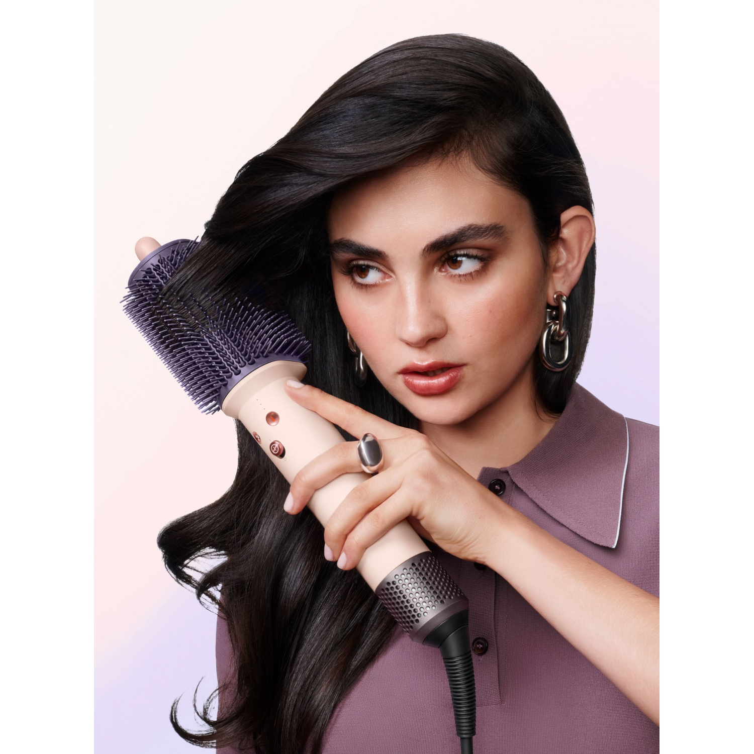 Una donna dai capelli castani modella la sua lunga chioma con una spazzola viola.
