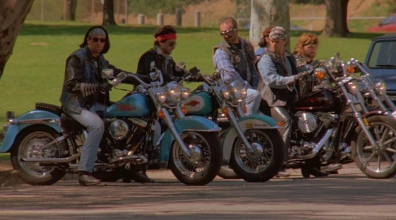 Gruppe von Männern sitzt auf Motorrädern in einem parkähnlichen Gelände.