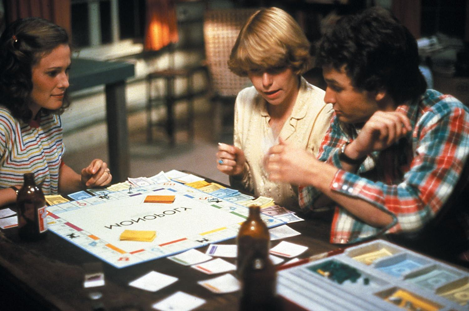 Drei junge Menschen sitzen an einem Tisch und spielen konzentriert ein Monopoly-Spiel.